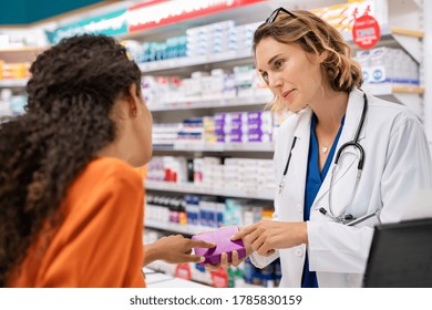 Pharmacist giving medicine box to customer in pharmacy. Doctor showing and explaining medicine dose to customer. Mature pharmacist giving advice on medicaments, while serving young african woman.  - Shutterstock ID 1785830159