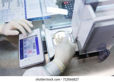 Pharmacist, a laboratory worker in sterile rubber gloves, weighs the manufactured tablets on the control scales. - Shutterstock ID 713066827