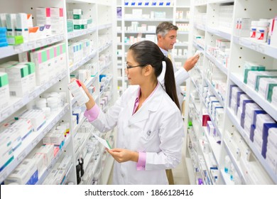 Un pharmacien avec une ordonnance qui regarde une boîte de médicaments sur une étagère de pharmacie. : photo de stock