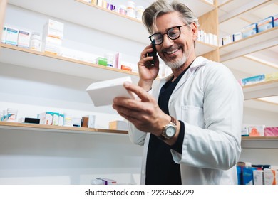 Pharmacist reading a medication label while talking to a patient on the phone. Senior healthcare worker confirming a prescription over a phone call. Mature man working in a clinic dispensary. - Powered by Shutterstock