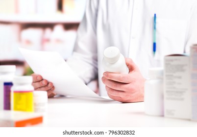 Pharmacist Reading Prescription With Medicine And Pill Bottle In Hand In Pharmacy. Medical Professional In Drugstore Counter. Clerk Or Druggist In Drug Store. Pharmaceutical Retail Business Concept.