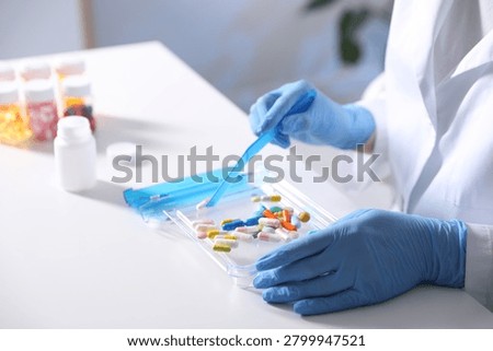 Pharmacist sorting different pills at white table in clinic, closeup