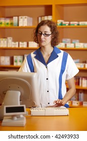 Pharmacist Typing On Computer Behind Pharmacy Counter