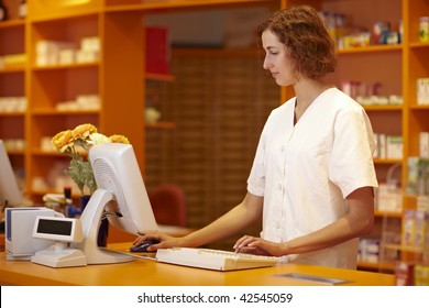 Pharmacist Typing On Computer Behind Pharmacy Counter