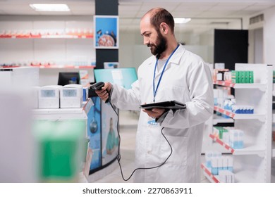 Pharmacist in white coat holding tablet computer typing products barcode while doing pills inventory in pharmacy. Drugstore worker is trained to recognize the various types of drugs and packages - Powered by Shutterstock