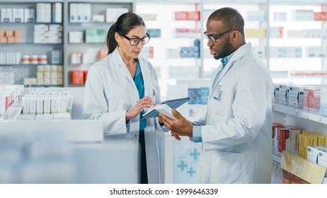 Pharmacy: Black Male And Caucasian Female Pharmacists Use Digital Tablet Computer Talk About Medicine, Drugs, Vitamins, Supplements, Vaccine, Health Care Products. Medical Professionals In Drugstore