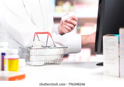 Pharmacy Cashier Or Clerk At Counter. Pharmacist Using Cash Register. Druggist With Pill Bottles In Shopping Basket In Drug Store. Sales Person Touching Electronic Payment System.