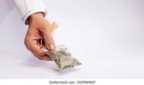 
Pharmacy Clerk Hands Over A Bag Of Medical Marijuana And Takes The Collection Money With The Other Hand, On A White Counter