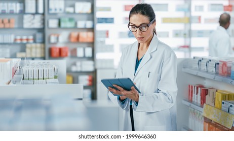 Pharmacy Drugstore: Beautiful Caucasian Pharmacist Uses Digital Tablet Computer, Checks Inventory Of Medicine, Drugs, Vitamins, Health Care Products On A Shelf. Professional Pharmacist In Pharma Store