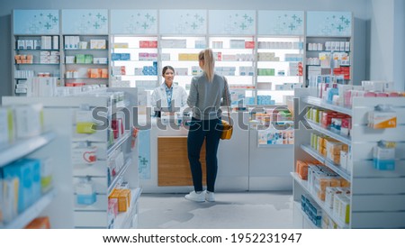 Pharmacy Drugstore: Beautiful Young Woman Buying Medicine, Drugs, Vitamins Stands next to Checkout Counter. Female Cashier in White Coat Serves Customer. Shelves with Health Care Products