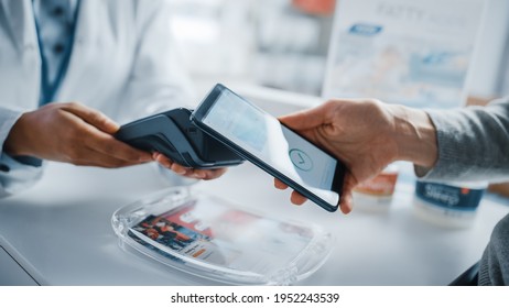 Pharmacy Drugstore Checkout Cashier Counter: Pharmacist and a Customer Using NFC Smartphone with Contactless Payment Terminal to Buy Prescription Medicine, Health Care Goods. Close-up Shot - Powered by Shutterstock