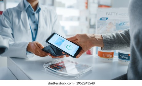 Pharmacy Drugstore Checkout Cashier Counter: Pharmacist and a Customer Using NFC Smartphone with Contactless Payment Terminal to Buy Prescription Medicine, Health Care Goods. Close-up Shot - Powered by Shutterstock