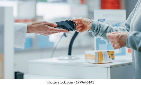 Pharmacy Drugstore Checkout Cashier Counter: Pharmacist and a Customer Using Contactless Credit Card with Payment Terminal to Buy Prescription Medicine, Health Care Goods. Close-up Focus on Hands