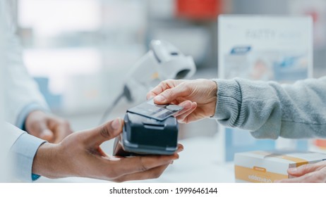 Pharmacy Drugstore Checkout Cashier Counter: Pharmacist and a Customer Using Contactless Credit Card with Payment Terminal to Buy Prescription Medicine, Health Care Goods. Close-up Focus on Hands - Powered by Shutterstock