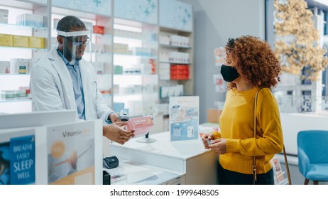 Pharmacy Drugstore Checkout Counter: Professional Black Pharmacist Wearing Face Shield Sells Medicine To Young Female Customer, Who Is Wearing Face Mask, Use Contactless Payment. Coronavirus Safety