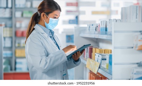 Pharmacy Drugstore: Portrait of Beautiful Pharmacist Wearing Face Mask Uses Digital Tablet Computer, Looks at Camera and Smiles Charmingly, Behind Her Shelves Full of Medicine Packages. Side View Shot - Powered by Shutterstock