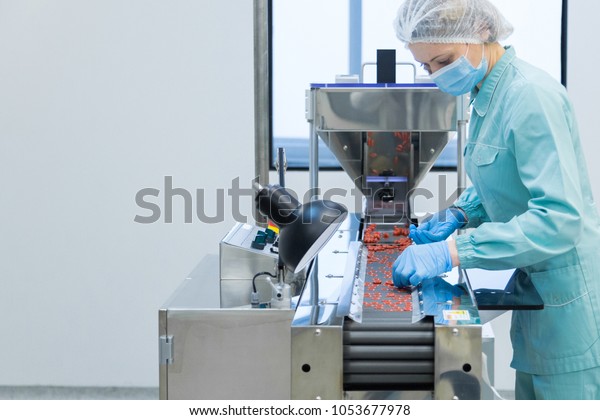 Pharmacy\
industry woman worker in protective clothing operating production\
of tablets in sterile working\
conditions