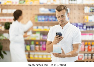 At pharmacy, man visitor with phone in hands scans QR code on box, photographs packaging and label of product, searches Internet for information about product - Powered by Shutterstock