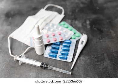 Pharmacy medicine, nasal spray, digital thermometer, syringe, pills in blister pack and medical mask on dark background. - Powered by Shutterstock