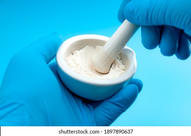 Pharmacy, pharmaceutical medication and medicinal preparation concept with pharmacist hands in gloves using mortar and pestle to ground fine white medicine blend isolated in science laboratory