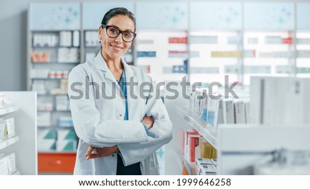 Pharmacy: Portrait of Beautiful Professional Caucasian Female Pharmacist Wearing Glasses, Crosses Arms and Looks at Camera Smiling Charmingly. Drugstore Store with Shelves Health Care Products