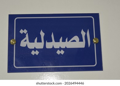 The Pharmacy Sign, An Arabic Door Sign On A Door In A Medical Center, Hospital,  The Translation Of The Sign ( The Pharmacy ), The Wall Sign Is Blue In Color And The Inscription Is White Colored 