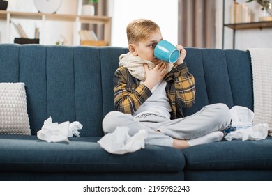 Pharyngitis, Sore Throat Concept. Sick Caucasian Teenage Boy Touching Sore Throat, Feeling Unwell, While Sitting On The Sofa At Home, And Drinking Hot Tea.