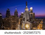 Philadelphia City Hall stands illuminated at dusk, with the William Penn statue overlooking the city’s vibrant skyline and modern skyscrapers under a colorful twilight sky.