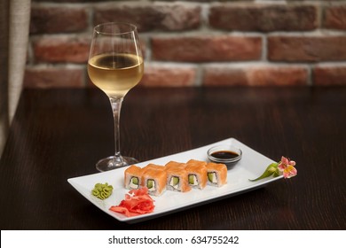 Philadelphia maki sushi rolls with salmon, cheese cream, cucumber on white plate and glass of wine.