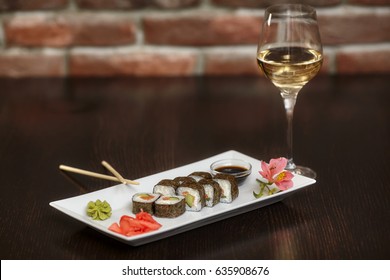 Philadelphia maki sushi rolls with salmon, cheese cream, cucumber on white plate and glass of wine