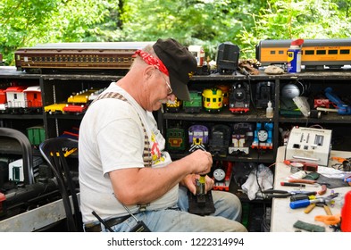 Philadelphia, PA / USA - 06-28-2013: Train Engineer Fixing A Model Train Surrounded By Collection Of Miniature Rail Cars.