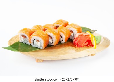 Philadelphia sushi rolls with salmon, rice, cream cheese, garnished with wild garlic, served with green wasabi paste, pickled ginger and lemon slices on a wooden board