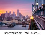 Philadelphia under a hazy purple sunset. An incoming train crosses Ben Franklin Bridge.