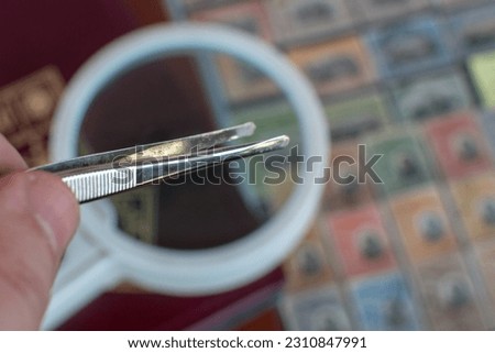 Philatelic tweezer , a loupe with faded stamps background