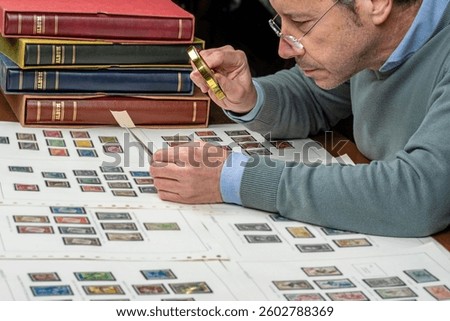 Philatelist examining and organizing postal stamp collection albums with magnifying glass.