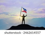 Philippines flag being waved by a man celebrating success at the top of a mountain against sunset or sunrise. Philippines flag for Independence Day.