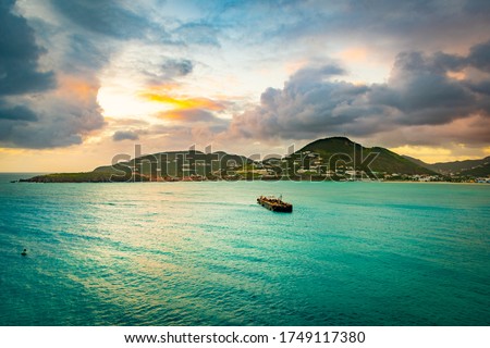 Philipsburg, Sint Maarten. Sunset ocean view in the Caribbean with cruise ship fuel bunker vessel sailing to coast. Mountains stretch along the coastline landscape with endless water all around.