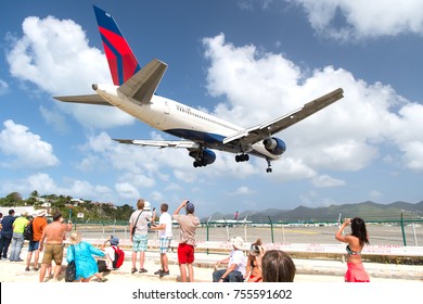 Philipsburg, St Maarten - February 13, 2016: People Watch Plane Land On Island Airport On Top Of Maho Beach Cloudy Blue Sky. 