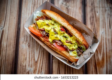 Philly cheese steak sandwich with meat, vegetables, cheese and sause in box on wooden table. street food