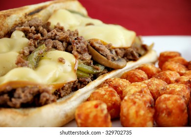 Philly cheese steak sandwich with potato puffs - shredded steak smothered with sauteed mushrooms, sauteed onions, sauteed green peppers, and Gouda cheese on a hoagie bun