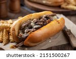 Philly cheesesteak sandwich made with steak, cheese and onions on a toasted hoagie roll with french fries on a wooden table