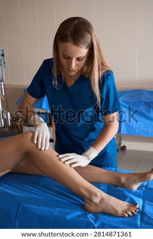 Phlebologist performs a physical examination on a female leg while the patient rests on a medical bed to check for varicose veins.