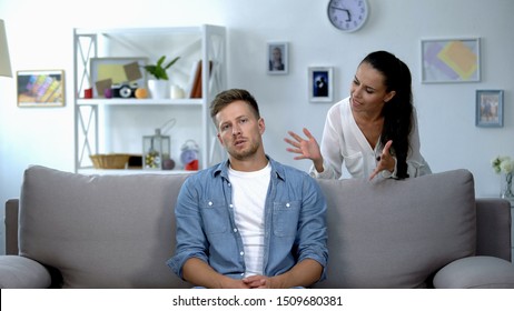 Phlegmatic man sitting on sofa listening nervous wife shouting, aggression