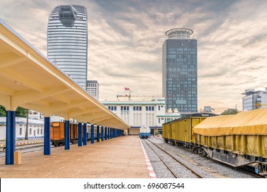 PHNOM PENH, CAMBODIA - February 03, 2017: A Yellow Freight Train Parking On The Rail Road With The Tow High Rises At The Background