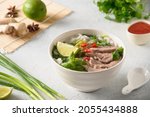 Pho Bo Soup with beef, rice noodles, ginger, lime, chili pepper in bowl on white background. Close up. Vietnamese and Asian cuisine.