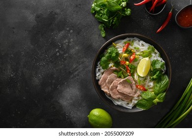 Pho Bo Soup With Beef, Rice Noodles, Ginger, Lime, Chili Pepper In Bowl On Black Background. View From Above. Copy Space. Vietnamese And Asian Cuisine.