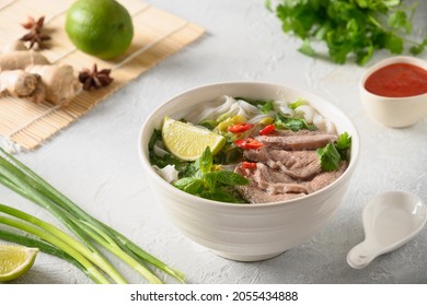 Pho Bo Soup With Beef, Rice Noodles, Ginger, Lime, Chili Pepper In Bowl On White Background. Close Up. Vietnamese And Asian Cuisine.