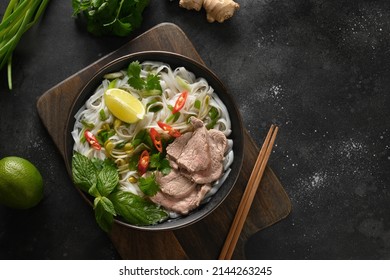 Pho Bo soup with beef, rice noodles, lime, chili pepper in bowl on black background. Vietnamese and Asian cuisine.
