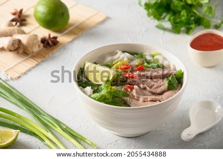 Pho Bo Soup with beef, rice noodles, ginger, lime, chili pepper in bowl on white background. Close up. Vietnamese and Asian cuisine.