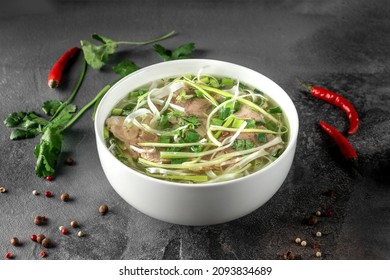 pho bo spicy broth or soup in white ceramic bowl with rice noodles, beef slices and herbs. concept of vietnamese food, side view